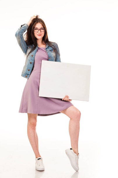 Young beautiful girl posing with white background for posting advertising, logo. Dressed in a pink dress and denim jacket, sneakers and glasses. Long hair. Isolated photo on the white background. - Fotografie, Obrázek