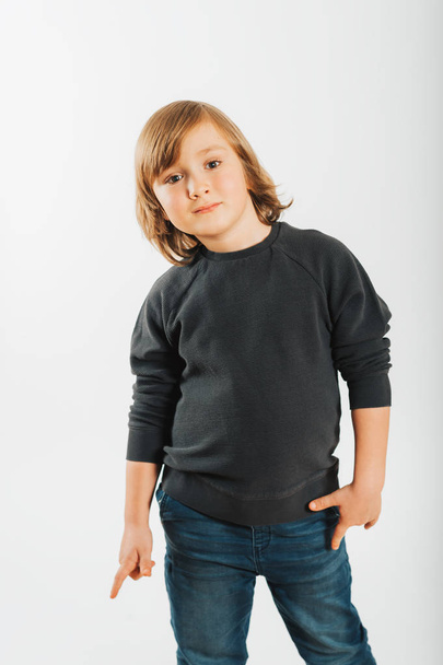 Студийный снимок очаровательного маленького мальчика с длинными светлыми волосами, в черной толстовке
 - Фото, изображение
