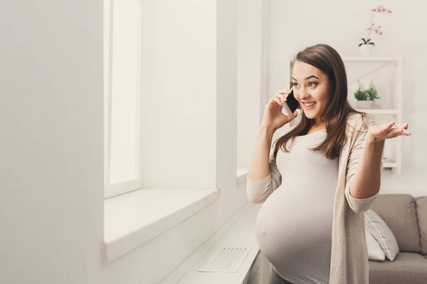 Усміхнена вагітна жінка говорить на своєму смартфоні
 - Фото, зображення