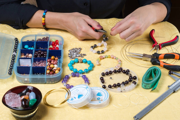 Tworzenie biżuterii. Kobiece ręce z narzędziem i kolorowe koraliki na żółtym tle. Selektywna koncentracja. - Zdjęcie, obraz