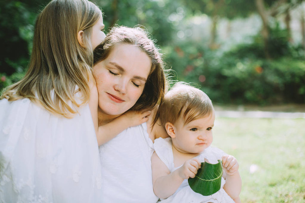 красивая молодая женщина обнимает своих маленьких дочерей в летнем парке
  - Фото, изображение