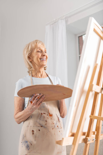 Glad mature woman enjoying her masterpiece - Фото, изображение