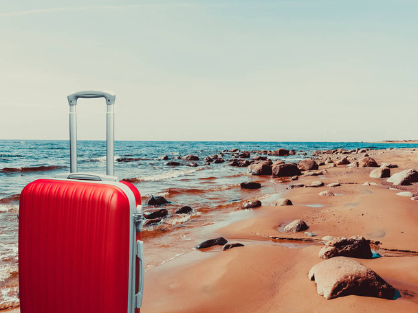 湾の海岸の砂に赤いスーツケース. - 写真・画像