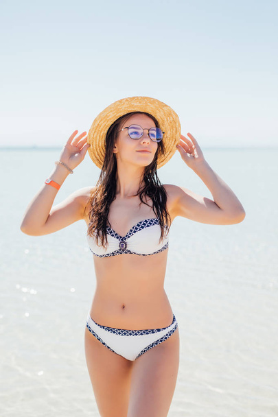 Femme heureuse sur la plage en lunettes de soleil et un chapeau de paille sur l'eau de mer bleue
 - Photo, image