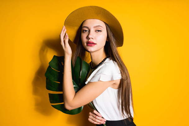 attractive young girl model in a hat posing, holds a green leaf - Foto, Imagen