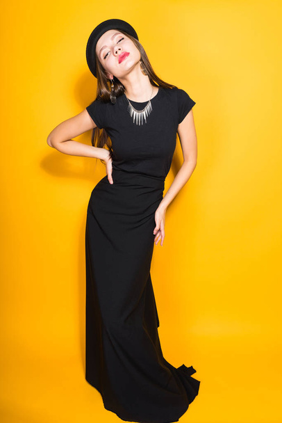 luxurious attractive woman in black dress and hat posing on yellow background - Foto, Imagem