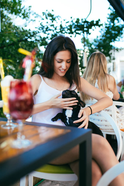 Beautiful young woman sitting in cafe with her adorable French bulldog puppy. People with dogs theme - Foto, Imagen