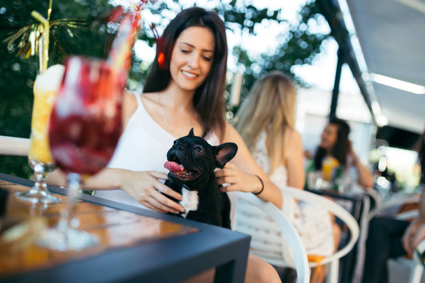 Beautiful young woman sitting in cafe with her adorable French bulldog puppy. People with dogs theme - Zdjęcie, obraz