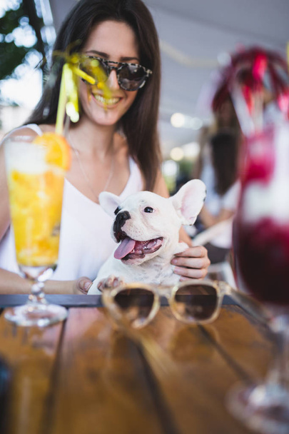 Beautiful young woman with sunglasses enjoying with her french bulldog puppy in cafe bar - Foto, immagini
