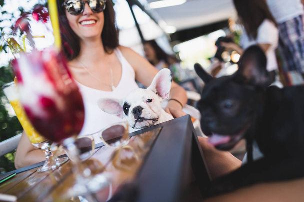 Beautiful young woman with sunglasses enjoying with her french bulldog puppy in cafe bar - Фото, изображение