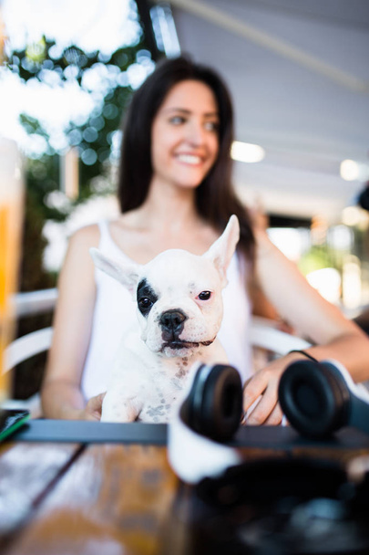 Beautiful young woman sitting in cafe with her adorable French bulldog puppy. People with dogs theme - Fotó, kép