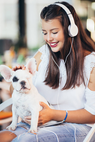 Beautiful young woman sitting in cafe with her adorable French bulldog puppy. Spring or summer city outdoors. People with dogs theme - Photo, Image