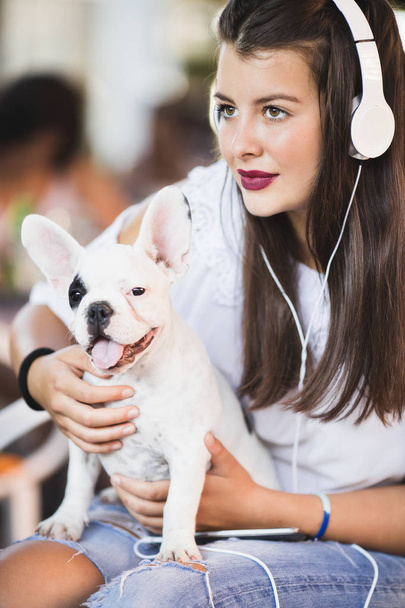 Beautiful young woman sitting in cafe with her adorable French bulldog puppy. Spring or summer city outdoors. People with dogs theme - 写真・画像