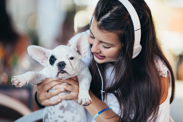 Beautiful young woman sitting in cafe with her adorable French bulldog puppy. Spring or summer city outdoors. People with dogs theme - 写真・画像