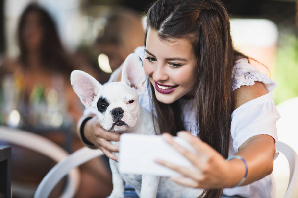 Beautiful young woman sitting in cafe with her adorable French bulldog puppy. Spring or summer city outdoors. People with dogs theme - Фото, зображення
