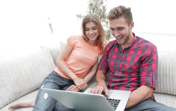 Счастливая современная пара серфингирует в сети и работает на ноутбуке дома - Фото, изображение