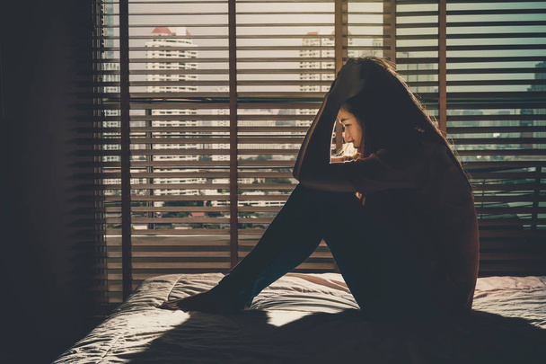 Femme déprimée assise et tendue sur le lit dans une chambre sombre avec un environnement de faible luminosité, concept dramatique
 - Photo, image