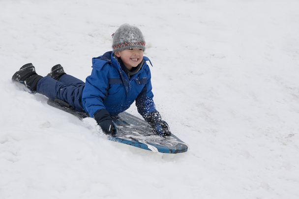 Мальчик скользит по снежному холму
. - Фото, изображение