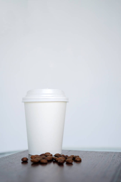 Eine Einwegbecher für Kaffee mit Kaffeebohnen steht auf einem Holztisch in einem Café. Seiten- oder Frontansicht mit Kopierraum - Foto, Bild