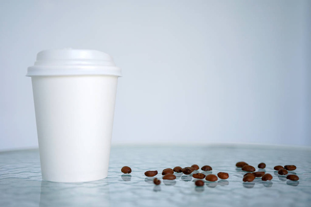 Kertakäyttöinen kuppi kahvia kahvipapuja, seisoo läpinäkyvällä pöydällä kahvilassa. Sivu- tai etunäkymä ja kopiotila
 - Valokuva, kuva