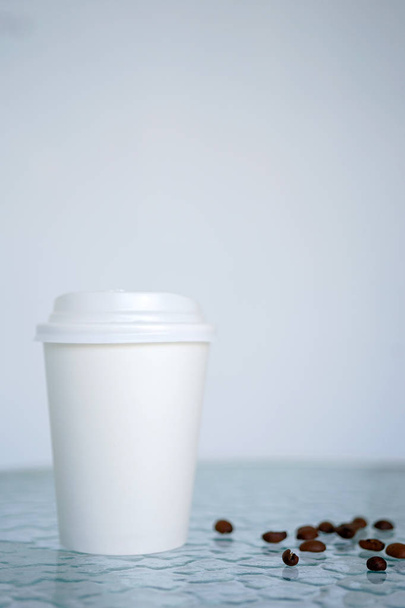 Une tasse jetable pour le café avec des grains de café, se tient sur une table transparente dans un café. Vue latérale ou frontale avec espace de copie
 - Photo, image