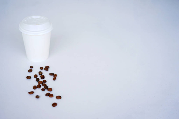 Uma xícara descartável para café com grãos de café, fica em uma telha branca. Vista superior com espaço de cópia
 - Foto, Imagem