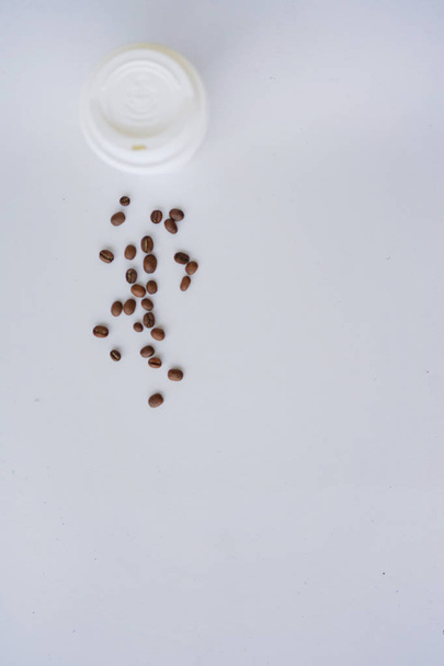Eine Einwegbecher für Kaffee mit Kaffeebohnen steht auf einer weißen Fliese. Ansicht von oben mit Kopierraum - Foto, Bild