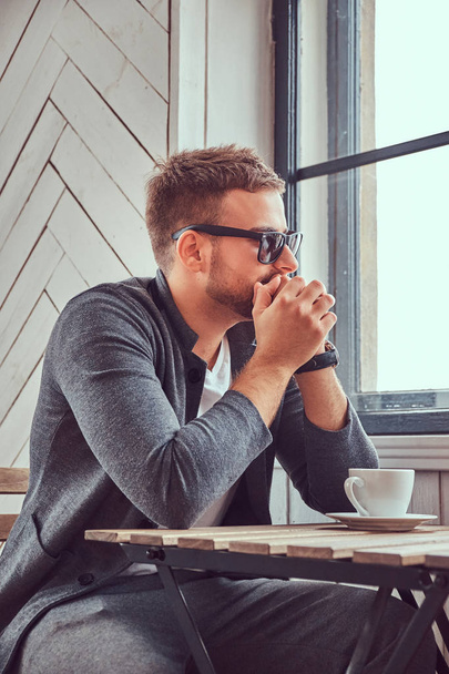 İçme kahve kahve dükkanında yakışıklı bir genç adam güneş gözlüğü ve rahat giysiler. - Fotoğraf, Görsel