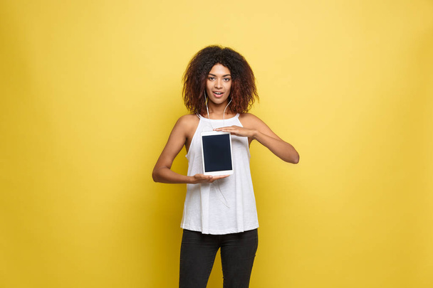 Lifestyle Concept - Portrait of beautiful African American woman joyful presenting something on electronic tablet. Yellow pastel studio background. Copy Space. - Foto, imagen