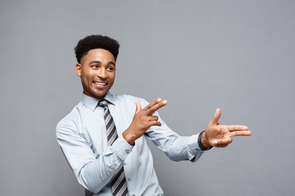 Business Concept - Cheerful happy young African American holding gun sign with fingers pointing to other.  - 写真・画像
