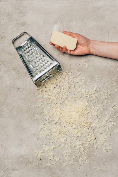 Close-up view of hand holding cheese by grater on light background - Фото, изображение