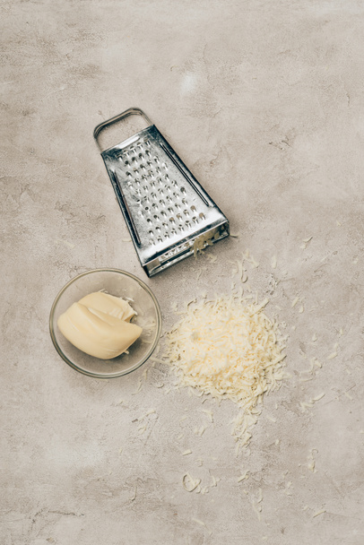 Grater and piece of cheese in bowl on light background - Φωτογραφία, εικόνα