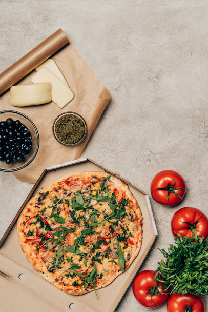 Whole pizza in cardboard box with tomatoes, cheese and olives on light background - Foto, Imagem