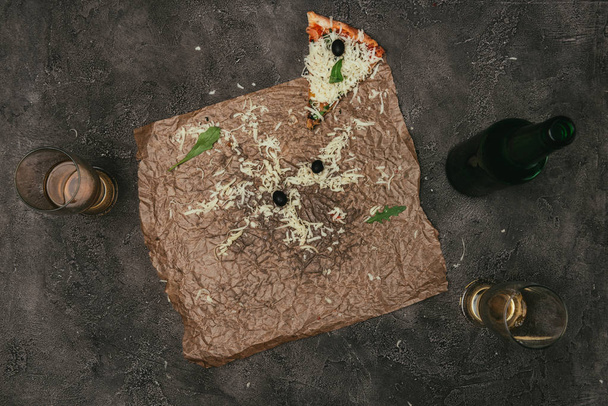Sobras de pizza sobre papel artesanal con cerveza sobre fondo oscuro
 - Foto, Imagen