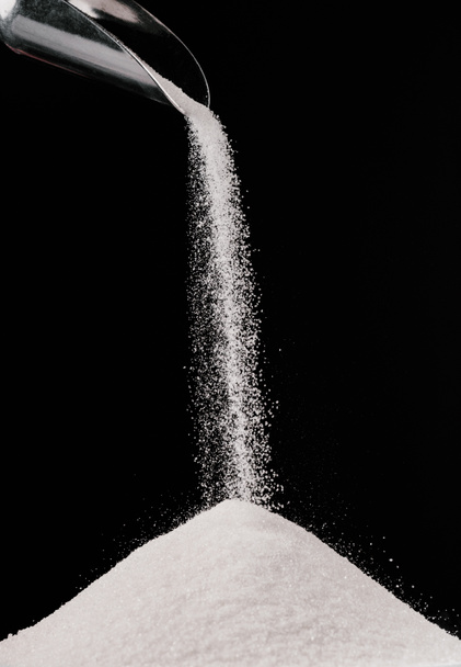 zucchero che cade da paletta di metallo su pila isolata su nero
 - Foto, immagini
