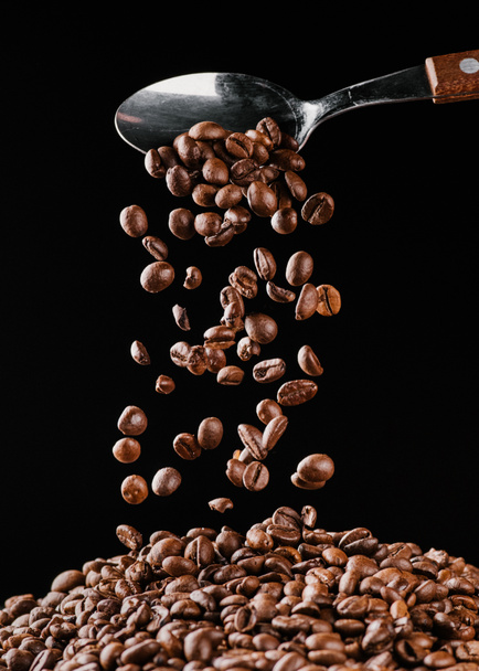 coffee beans falling from spoon on pile isolated on black - Photo, Image