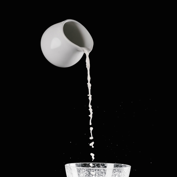 mleko leje z jar mleka do miski z mąką na czarnym tle - Zdjęcie, obraz