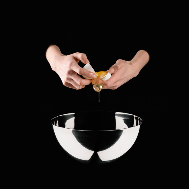 cropped image of woman holding broken chicken egg above bowl isolated on black - Foto, immagini