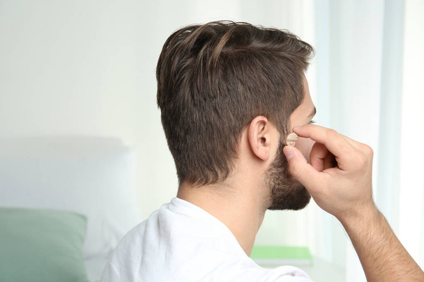 Young man putting hearing aid in ear indoors - Foto, Imagen