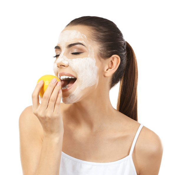 Beautiful young woman with facial mask eating ripe lemon on white background - Фото, зображення