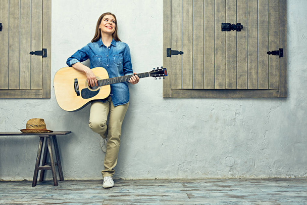Positive woman playing guitar while standing near light wall - Foto, Imagem