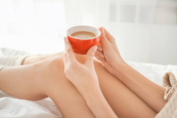 Young woman with cup of coffee on bed at home - Photo, Image