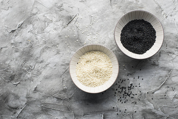 White and black sesame in the same ceramic bowls on a gray background. Top view. Copy space. - Zdjęcie, obraz