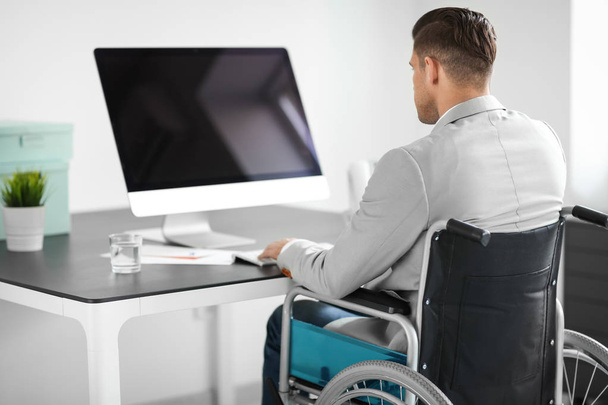 Young man in wheelchair at workplace - Фото, зображення