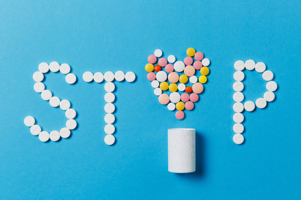 Medication white, colorful round tablets in word Stop isolated on blue background. Pills heart shape, letter, bottle. Concept of health, treatment, choice, healthy lifestyle. Copy space advertisement. - Foto, Imagem