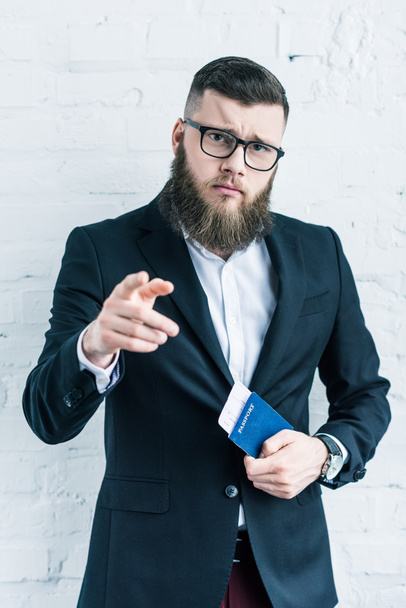 portrait of businessman with passport and ticket in hand pointing at camera - Valokuva, kuva