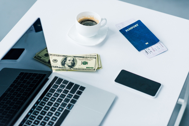 close up view of laptop, smartphone, money, cup of coffee and passport with ticket on tabletop - 写真・画像