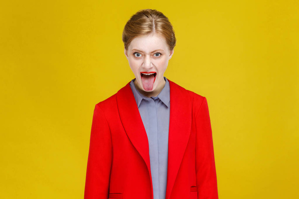 crazy redhead businesswoman in red jacket looking at camera and showing tongue out  - Фото, изображение