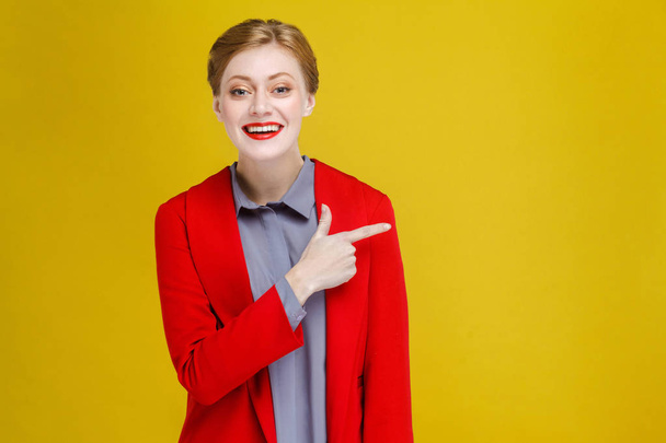 redhead businesswoman in red jacket showing at copy space on yellow background - Zdjęcie, obraz