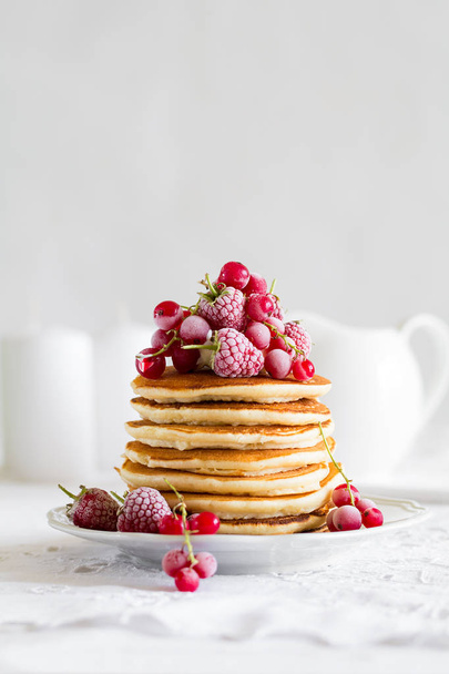 Stack of pancakes with raspberry, red currant, cream and honey on white table cloth - Фото, изображение